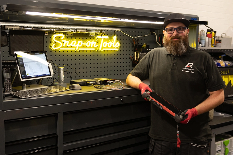 Machanic leans against work station holding diagnostic iPad